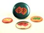 Vier runde Ansteckbuttons mit Foliendruck Veredlung mit stilisierten Blattmotiven in Herbstfarben liegen auf einer hellen Oberfläche. Der größte Button steht aufrecht, während die anderen flach liegen.